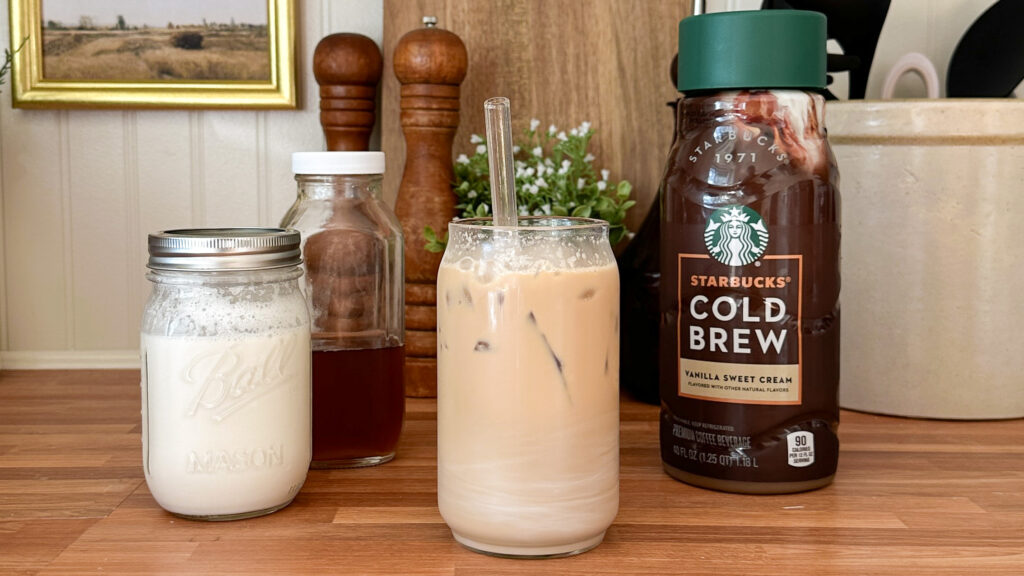 Glass of coffee on counter with cream, vanilla, and cold brew next to it